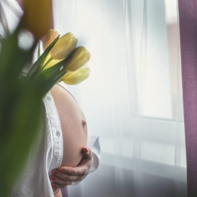 pregnant girl holding flowers. pregnant woman standing by the window with flowers.